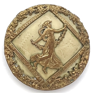 Brass button of a dancing woman over some sort of natural material.