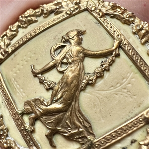 Brass button of a dancing woman over some sort of natural material.