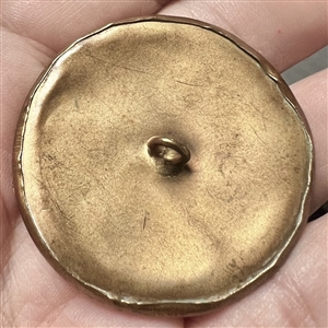 Brass button of a dancing woman over some sort of natural material.