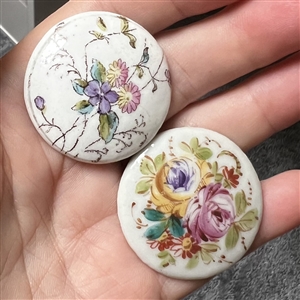 Two painted porcelain buttons of flowers.