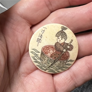 Incised and inked natural material button an Asian child in a small boat.