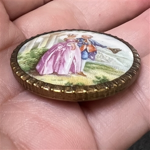 Transfer and painted porcelain button of a man and woman viewing land. 
